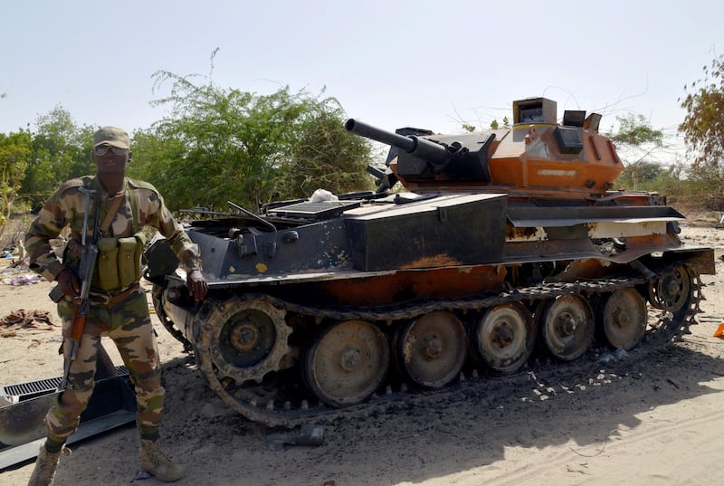 A soldier from the Niger army stands next to a burnt out  tank belonging to the Boko Haram militants, on May 25, 2015 in Malam Fatori, in northern Nigeria, near the border with Niger, where the Niger and Chadian army troops, are working together in support of Nigerian forces, to fight the Boko Harm Islamists. Boko Haram, which wants to create a hardline Islamic state in northeast Nigeria, has been pushed out of captured towns including Malam Fatori, and territory, since February by Nigerian troops with assistance from Niger, Chad and Cameroon. AFP PHOTO / ISSOUF SANOGO (Photo by ISSOUF SANOGO / AFP)
