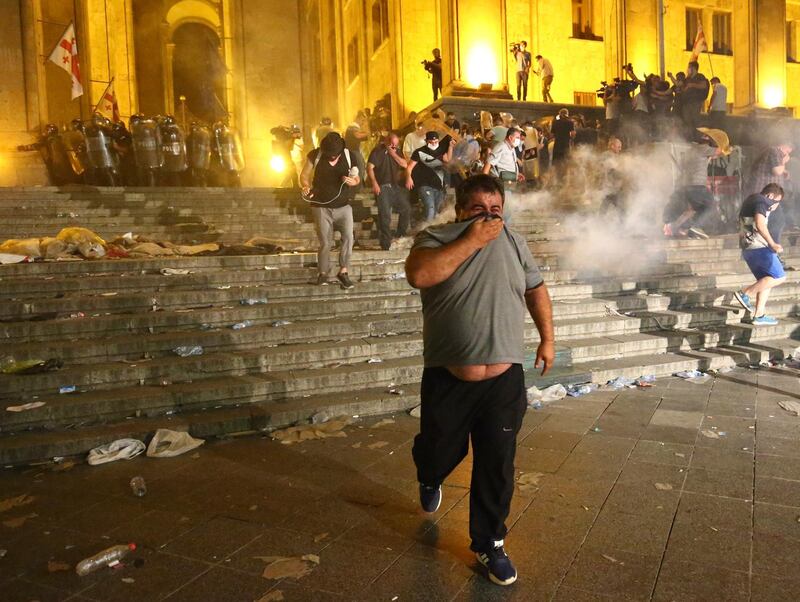 Opposition demonstrators run away as police fired a volley of tear gas against them at Georgian Parliament during a protest in Tbilisi, Georgia, Friday, June 21, 2019. Police have fired a volley of tear gas at a massive throng of protesters outside the Georgian national parliament, who are trying to storm the building and are demanding the government's resignation. (AP Photo/Zurab Tsertsvadze)