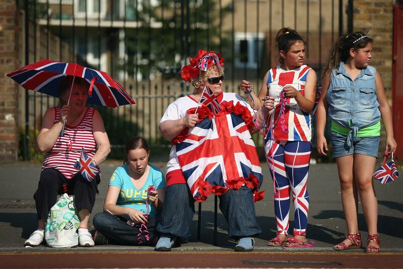 LONDON, ENGLAND - JULY 25:  Members of the public gather to watch Torchbearer Scott Moorhouse, a Paralympic javelin thrower running with the Olympic flame along Tottenham High Road past the remnants of a branch of carpet retailer Carpet Right that was burnt down during last year's riots on July 25, 2012 in London, England. The Olympic flame is making its way through the capital's Northern boroughs on day 68 of its journey around the UK before arriving in the Olympic Stadium on Friday evening for the Olympic games' Opening Ceremony.  (Photo by Dan Kitwood/Getty Images)