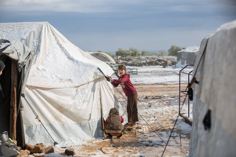 A child and her sister try to cover their tent, which was destroyed by a snowstorm in northern Syria.