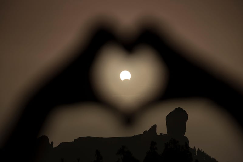 A woman makes a heart shape with her hands during a partial eclipse of the sun over the 'Roque Nublo' mountain at the Canary Island of Gran Canaria, Spain. Borja Suarez / Reuters