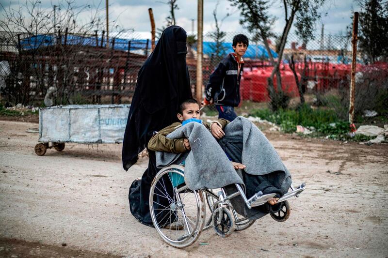 A woman pushes a boy on a wheelchair in al-Hol camp. AFP