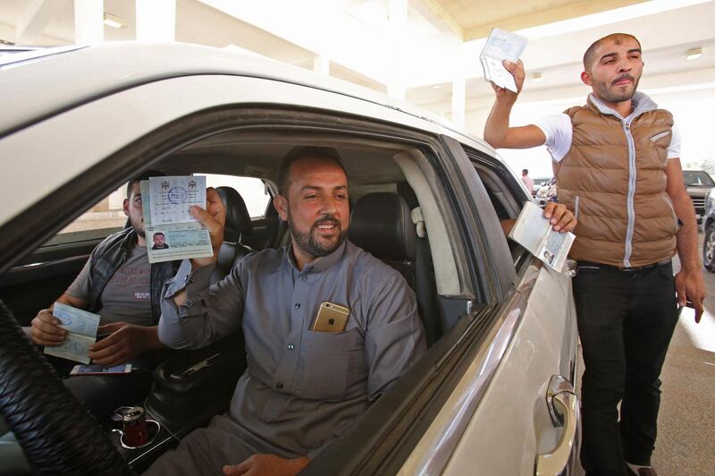 This picture taken from the Jordanian Mafraq governate on Ocotber 15, 2018, shows Jordanian men showing their passport at the Jaber border crossing between Jordan and Syria (Nassib crossing on the Syrian side) on the day of its reopening. The main border crossing between Jordan and war-torn Syria reopened on October 15 after a three year closure, an AFP photographer reported. The black metal border gate was opened from the Jordanian side of the crossing at 8:00 am (0500 GMT) as more than a dozen police and customs officials stood nearby, the photographer said, while several cars bearing Jordanian license plates queued on the Syrian side ready to roll in. / AFP / Khalil MAZRAAWI
