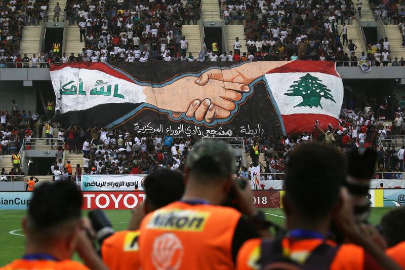 Football fans hold a large banner bearing the colours of the Lebanese (R) and Iraqi flag during the AFC Cup football match between Al-Zawraa and Al-Ahed at the Karbala Sports City stadium on April 10, 2018. 
Iraq is hosting a foreign football club for a competitive match for the first time in decades, after FIFA gave the go-ahead for games to resume. / AFP PHOTO / Mohammed SAWAF