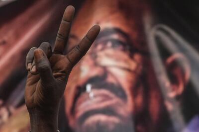 (FILES) In this file photo taken on April 19, 2019, a Sudanese protester flashes a victory sign in front of a banner depicting ousted and detained president Omar al-Bashir, during a protest outside the army headquarters in the capital Khartoum.  A year after one of Africa's longest serving leaders, Omar al-Bashir, was ousted from power in the face of mass street protests, Sudan is still reeling from daunting crises including deep economic woes. Bashir was overthrown on April 11, 2019 by the military, which was responding to mounting public anger against his three decades of iron-fisted rule. / AFP / OZAN KOSE

