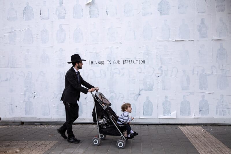 An Orthodox Jew with his child passes by a building wall in central Tel Aviv where white paint was used to try to cover up the many portraits of male African asylum seekers that were held in the Holot detention Center in southern Israel , photographed by several  Israeli photographers and displayed in several places to cause awareness about the Israeli government's plan to deport thousands .(Photo by Heidi Levine for The National).