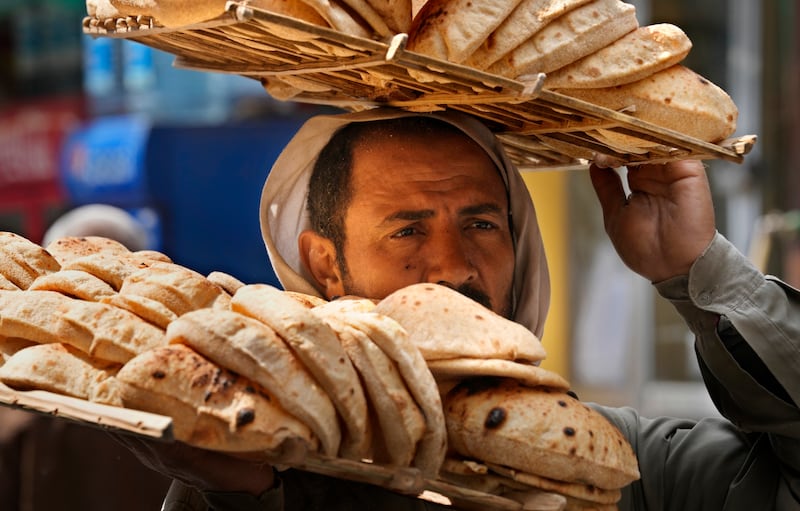 A bread vendor carries a tray of traditional Egyptian 'baladi' flatbread outside a Cairo bakery. The Russia-Ukraine war has caused soaring food prices and supply chain disruptions in the North African country. AP