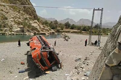 Onlookers stand next to a damaged bus at the site of an accident in a remote district of Balochistan province on June 11, 2021. A bus carrying dozens of pilgrims plunged into a ravine in southwest Pakistan on June 11 killing at least 18 passengers, officials said. / AFP / -
