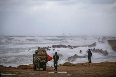 A Palestinian walks with his donkey-drawn cart loaded with collected junk along the Mediterranean seashore during stormy weather in Gaza City on February 17, 2021. / AFP / Mohammed ABED