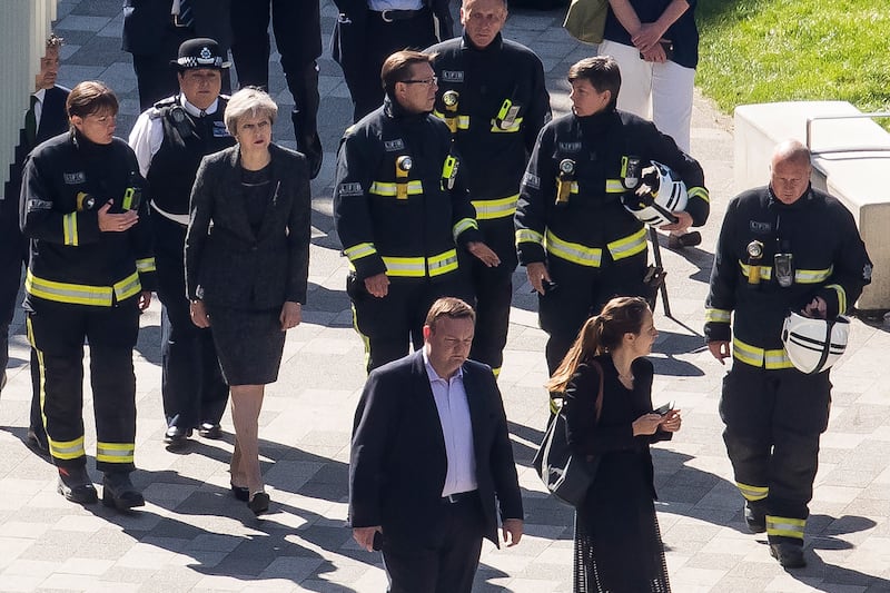Members of the fire service join Ms May on a visit to Grenfell Tower in London, in June 2017, the day after at least 12 people were confirmed dead and dozens missing after the 24-storey tower was engulfed in flames