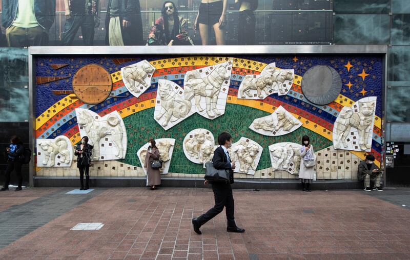 A man wearing a face mask to help curb the spread of the coronavirus walks past a mural displayed at Shibuya station in Tokyo. The sculpture in relief titled "Hachiko Family" was designed by Ryutaro Kitahara and sculpted by Louis Fransen. AP Photo