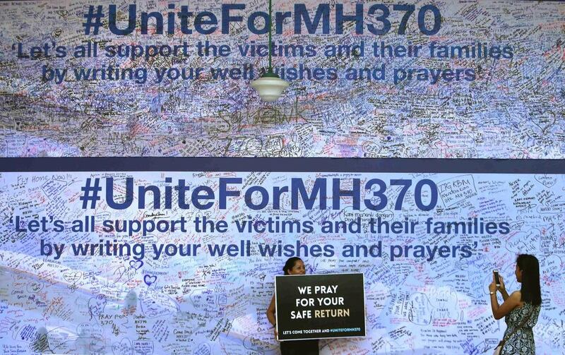 Visitors take pictures with a placard against the backdrop of a board dedicated to passengers onboard the missing Malaysia Airlines Flight MH370 and their families, in Petaling Jaya. Samsul Said / Reuters