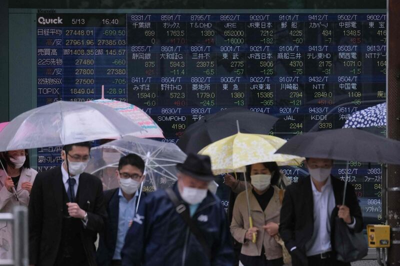 Pedestrians cross a road in front of an electronic quotation board displaying the numbers of company stock prices on the Tokyo Stock Exchange in Tokyo on May 13, 2021. / AFP / Kazuhiro NOGI
