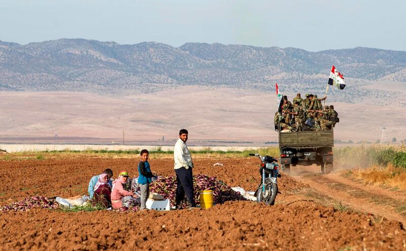 Syrian government soldiers ride in the back of a truck with national flags past people sitting in a field with harvested aubergines, as government forces deploy for the first time in the eastern countryside of the city of Qamishli in the northeastern Hasakah province. AFP