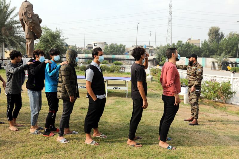 Patients line up as fighters from Iraqi Shiite armed group Saraya al-Salam (Peace Brigades) stand guard