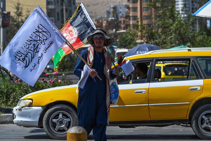 An Afghan street vendor carries Afghanistan national flags and Taliban flags to sell at a street intersection in Kabul. AFP