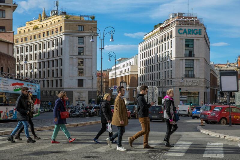 Pedestrians cross the street near a Banca Carige SpA bank branch in Rome, Italy, on Monday, Feb. 4, 2019. A manufacturing and export-led slump in Italy's economy spilled into services at the start of the year, aggravating an already fragile economic situation in the euro area. Photographer: Alessia Pierdomenico/Bloomberg