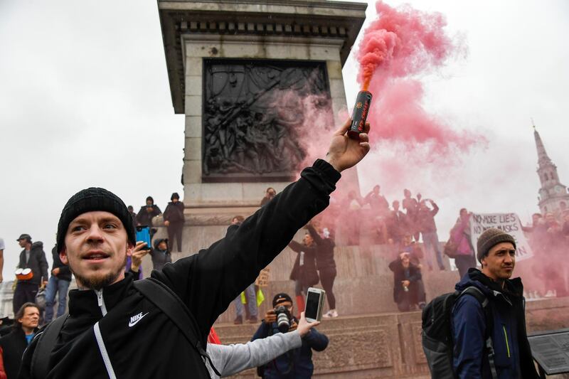 A protestor holds a flare, in Trafalgar Square, during a coronavirus anti-lockdown protest, in London, Saturday, Oct. 24, 2020. (AP Photo/Alberto Pezzali)