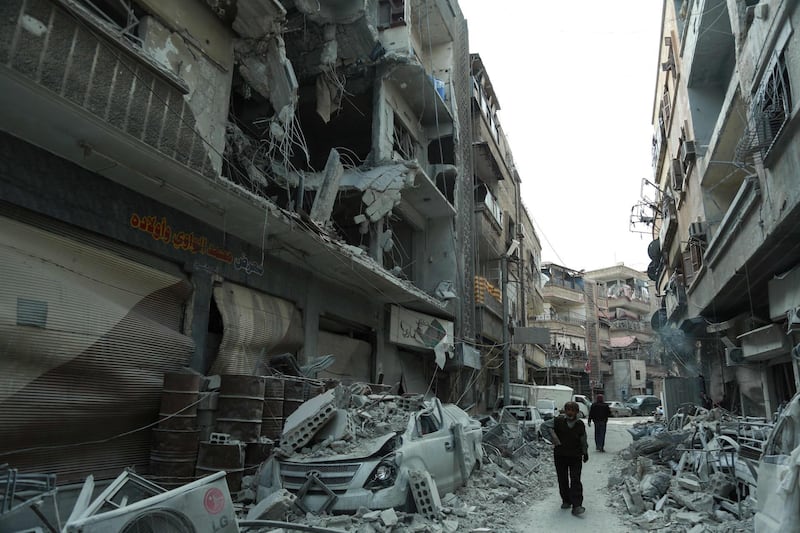 A picture taken on March 8, 2018 shows Syrians walking down a street past rubble from destroyed buildings, in the rebel-held town of Douma in the Eastern Ghouta enclave on the outskirts of Damascus. / AFP PHOTO / HAMZA AL-AJWEH