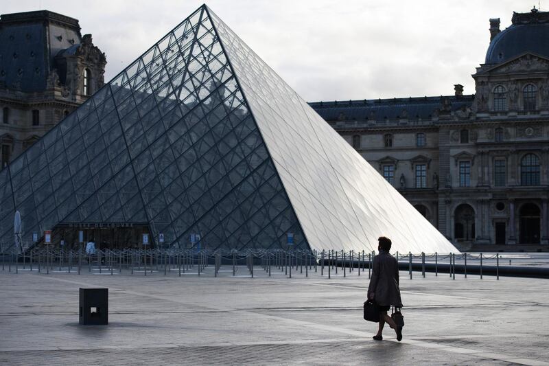 A pedestrian crosses the empty courtyard outside the Louvre Museum during morning rush hour in Paris. Bloomberg