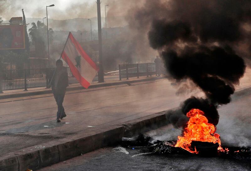 A Lebanese protester walks past burning tyres during ongoing anti-government demonstrations in Beirut.  AFP