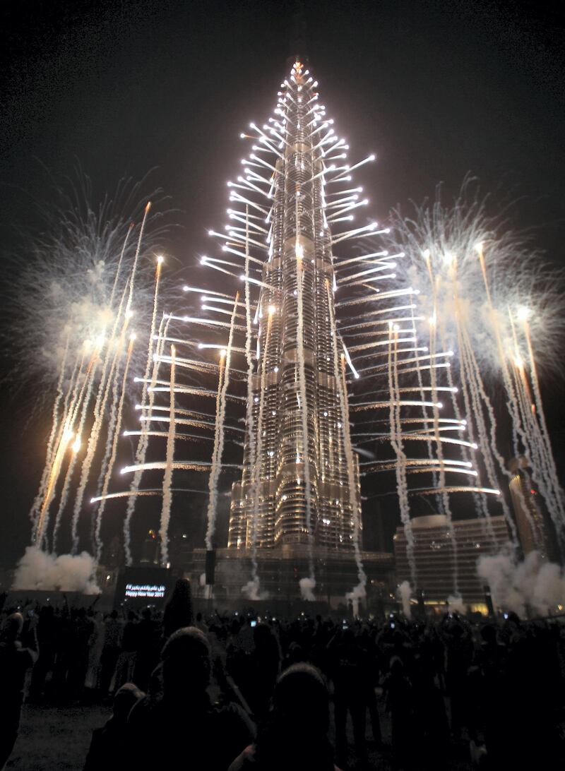 Crowds look at fireworks bursting around Burj Khalifa, the tallest building in the world, marking the New Year at midnight on January 1, 2011 in the Gulf emirate of Dubai. AFP PHOTO/KARIM SAHIB (Photo by KARIM SAHIB / AFP)