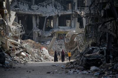 Palestinians walk among destroyed buildings as they return to Khan Younis. EPA