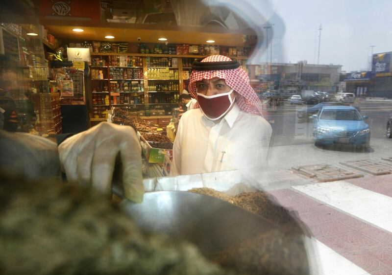 A man wearing a face mask as a precaution against the spread of the coronavirus is reflected in the window of a store as he buys herbs in Jiddah. AP