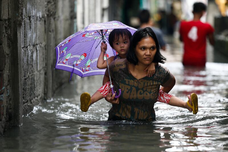 A woman carries a child on her back as they go through floodwaters in Quezon City, east of Manila. Rolex De La Pena / EPA