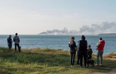 Fuel tanks ablaze as people watch damaged sections of the Kerch bridge in the Kerch Strait, Crimea, October 8, 2022. Reuters