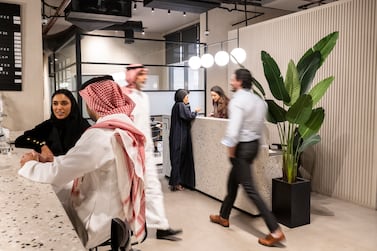 Mixed-age business people in traditional Saudi and western attire relaxing at coffee bar, walking through lobby, and talking at reception desk. Getty Images