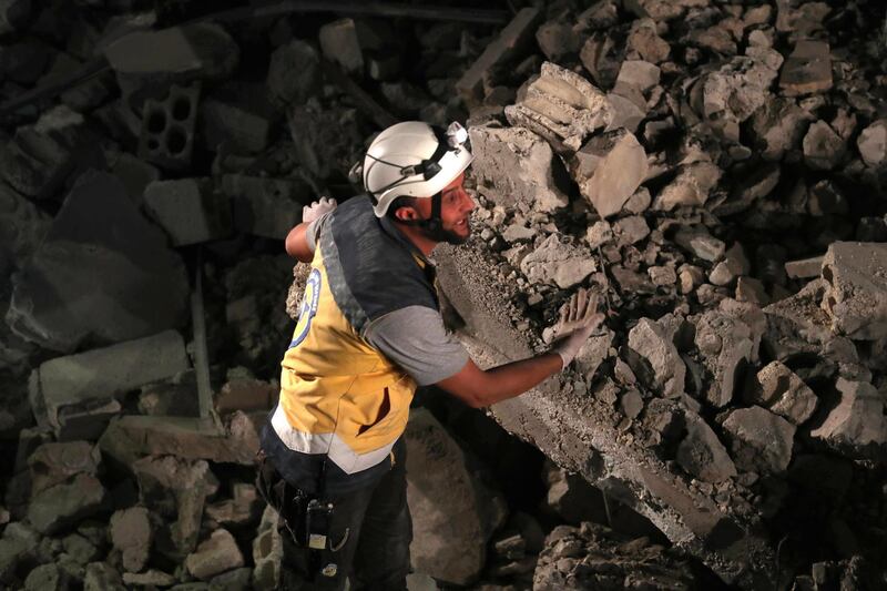 A member of the Syrian Civil Defence, also known as the "White Helmets", gesture as rescuers attempt to clear debris while searching for bodies or survivors in a collapsed building following a reported government air strike in the village of Saraqib in Syria's northwestern Idlib province.