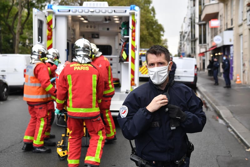 A police officer stands guard as firefighters lift an injured person into an ambulance. AFP