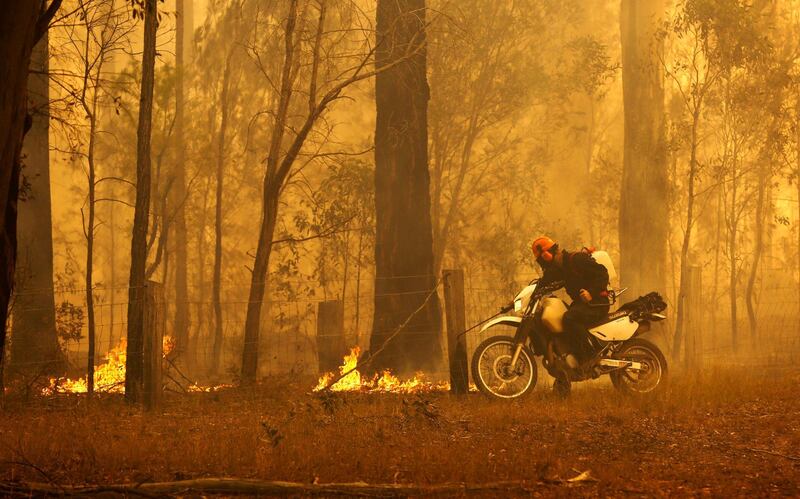 A resident puts out small fires as he rides his motorcycle in Old Bar, New South Wales, Australia.  EPA