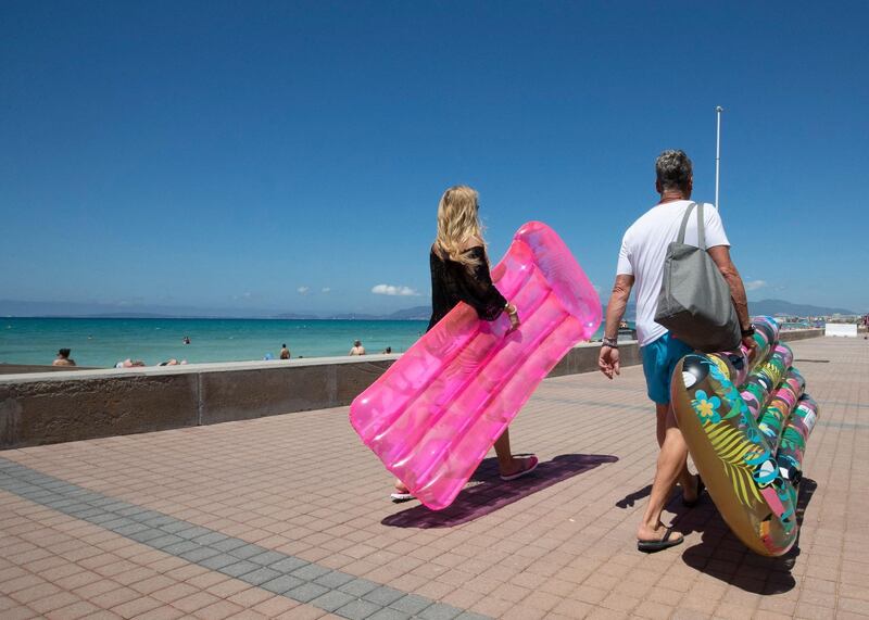 Tourists walk with inflatable mattress at Palma Beach in Palma de Mallorca. AFP