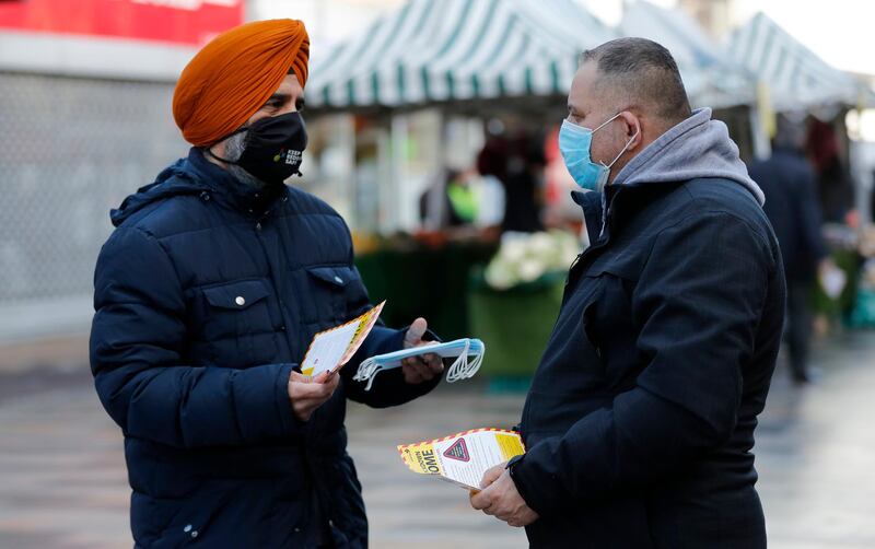 Redbridge Councillor Jas Athwal, left, hands out leaflets and speaks to pedestrians in the town centre of Ilford. AP Photo