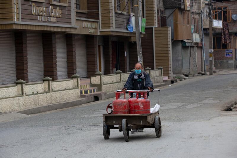 A Kashmiri laborer pushes a hand card filled with cooking gas cylinders before delivering them during a lockdown in Srinagar. AP