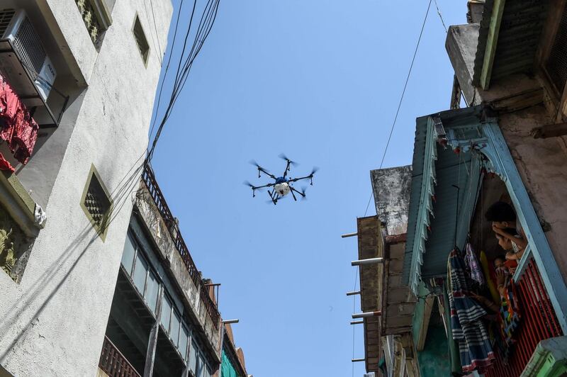Local residents (R) watch from their balcony a drone operated by a personnel from Ahmedabad Fire and Emergency Services spraying disinfectant in a residential area during a government-imposed nationwide lockdown as a preventive measure against the COVID-19 coronavirus, in Ahmedabad on May 9, 2020. / AFP / SAM PANTHAKY
