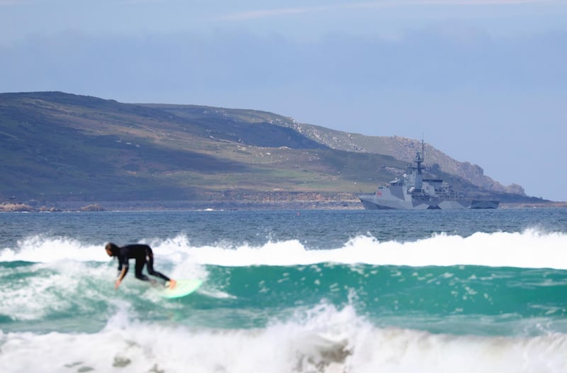A surfer catches a wave in front of a naval vessel in St Ives Bay. Reuters