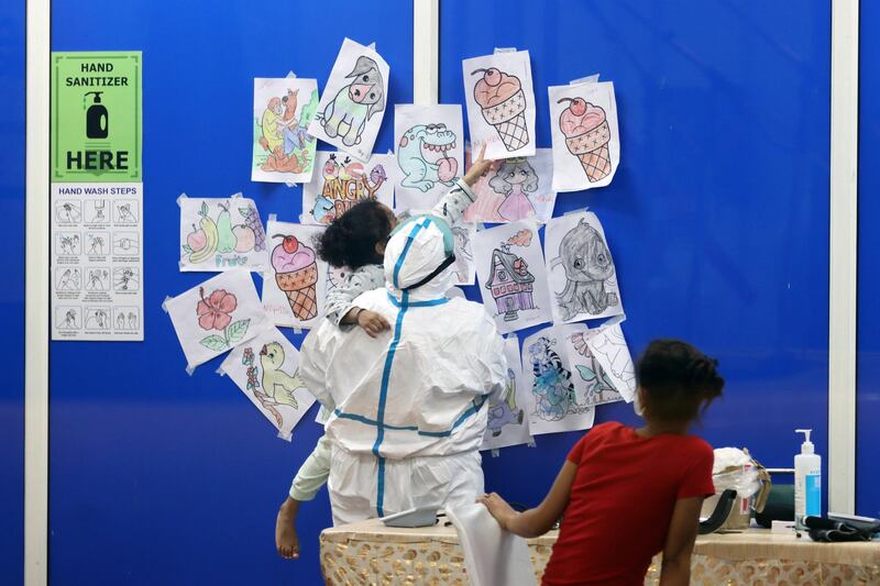 A health worker holds a child as they look at coloring sheets on a wall at the Covid-19 Care Center set up at the Commonwealth Games Village Sports Complex in New Delhi, India. Bloomberg