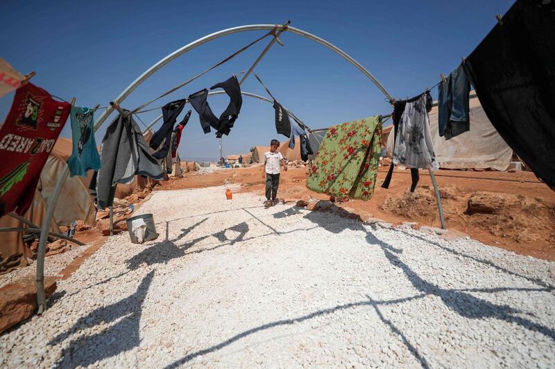 A displaced Syrian boy stands next to clothes at a camp near the town of Maaret Misrin in Syria's northwestern Idlib province. AFP