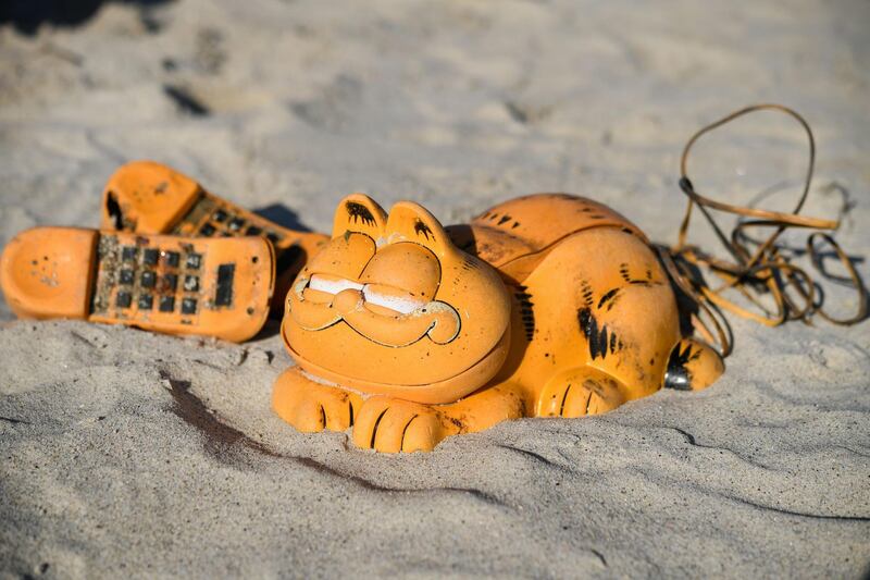 Spare parts of plastic 'Garfield' phones are displayed on the beach on March 28, 2019 in Plouarzel, western France, after being collected from a sea cave by environmental activists. For more than 30 years, plastic phones in the shape of the famous cat 'Garfield' have been washing up on French beaches. The mystery is now solved : a shipping container which washed up during a storm in the 1980s, was found in a hidden sea cave. / AFP / Fred TANNEAU
