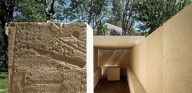 A sandy stone slab by Eduardo Souto de Mour of Portugal. The minimal design of maximum proportions is an enclosure of four thick walls of roughly finished travertine with a stone table inside for an altar and a ledge where congregants can sit.