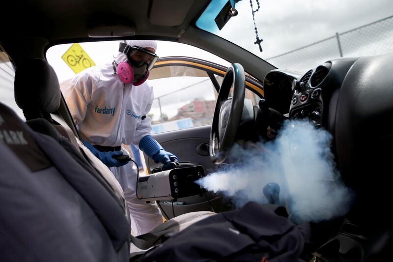 A cleaning employee using protective gear disinfects the interior of a taxi in Bogota, Colombia. Reuters