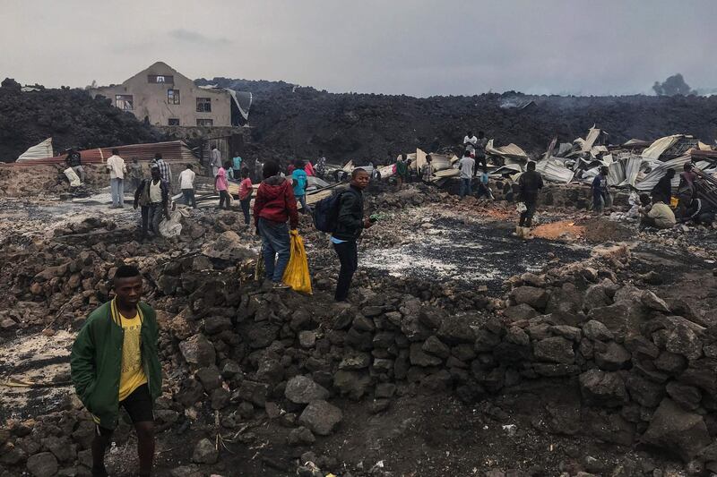 Residents are seen standing next to destroyed structures near smouldering ashes early morning in Goma in the East of the Democratic Republic of Congo following the eruption of Mount Nyiragongo. AFP