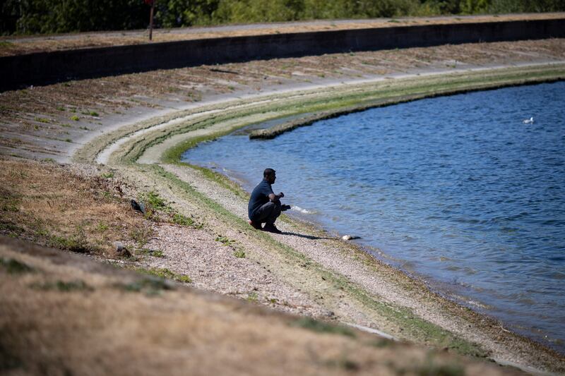 A person sits by a reservoir with low water levels and dried grass at Walthamstow Wetlands in London, England. EPA