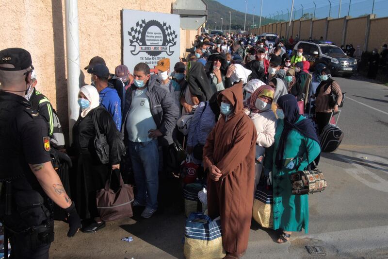 A Spanish National Police officer stands guard as several Moroccan citizens wait in line for repatriation. EPA