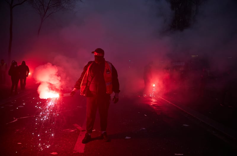 Yellow vests and railway workers walk towards French riot police holding flares amid violent clashes between officers and protesters during a rally near Place de Republique, in support of a national strike in France in December 2019.
