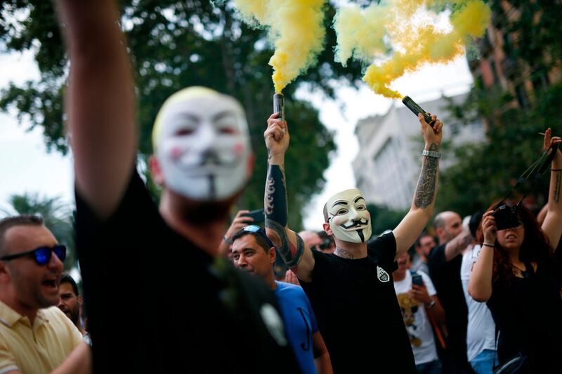 A protester wearing a Guy Fawkes mask lights flares during a strike by taxi drivers in Barcelona.  AFP / Pau Barrena