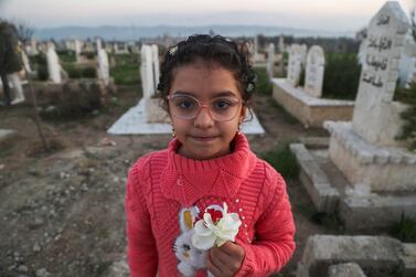 Syrian earthquake survivor Yasmine al-Sham carries flowers while posing for a picture in a cemetery where earthquake victims were buried in Jindayris town in the northwest of Aleppo province on February 2, 2024.  On February 6, 2023, a devastating quake ravaged Turkey and Syria, killing more than 1,400 people in government-controlled areas of Syria, while more than 4,500 died and tens of thousands were injured in areas held by opposition factions in the country's northwest according to Damascus.  Jindayris, in Aleppo province near the border with Turkey, was one of the areas worst-hit.  (Photo by Aaref WATAD  /  AFP)